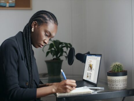 A woman in a blue sweater writes on a tablet at a desk