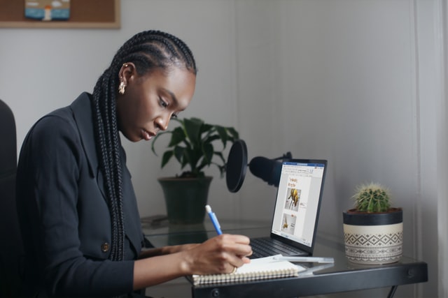 A woman in a blue sweater writes on a tablet at a desk