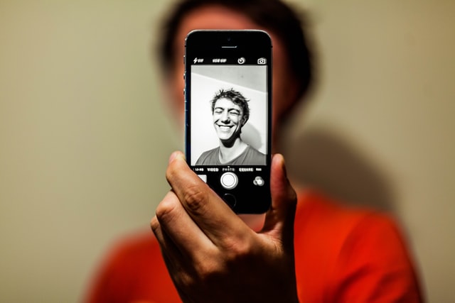 A smartphone taking a picture of a smiling man in a t-shirt.