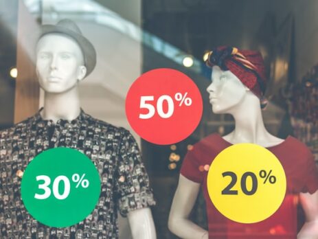 Two mannequins in a shop window with discount offers.