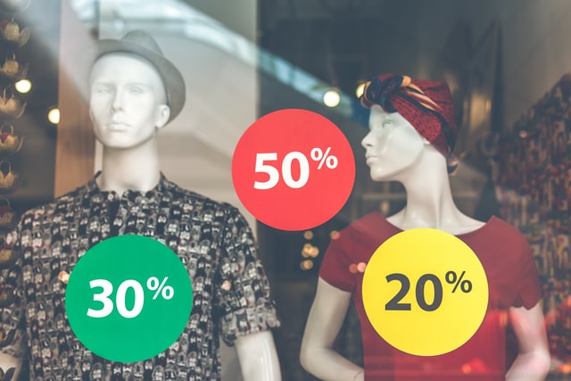 Two mannequins in a shop window with discount offers.