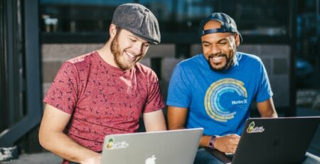 Two men sitting laughing as they work on laptop computers.