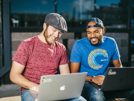 Two men sitting laughing as they work on laptop computers.