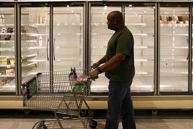 A man pushes a shopping cart past empty store shelves.