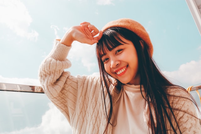 A young woman in a yellow beanie smiles at the camera in the sunshine.