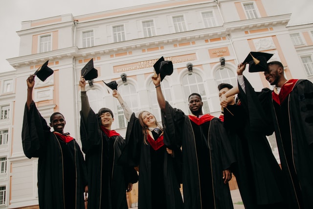 Six university graduates lift their caps and smile for the camera.