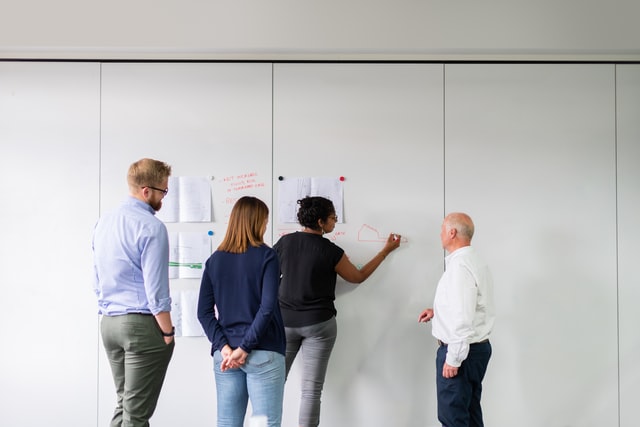 A woman points at writing on a wall during a brainstorming session.