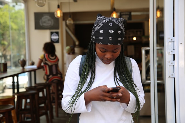 A young woman stands in a doorway scrolling on a smartphone.