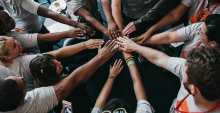 A large group of people with their hands joined at the center of a circle.