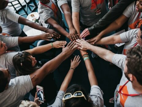 A large group of people with their hands joined at the center of a circle.