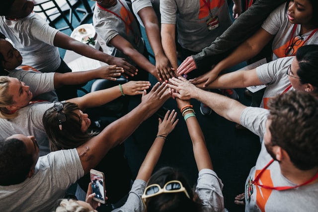 A large group of people with their hands joined at the center of a circle.