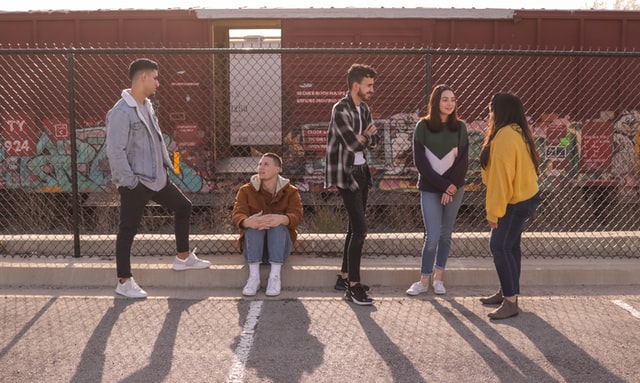 Five friends hang out near a chain-link fence.