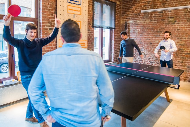 A group of men plays ping-pong in a bright room.