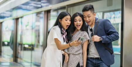 Three people act surprised as they look at a smartphone.