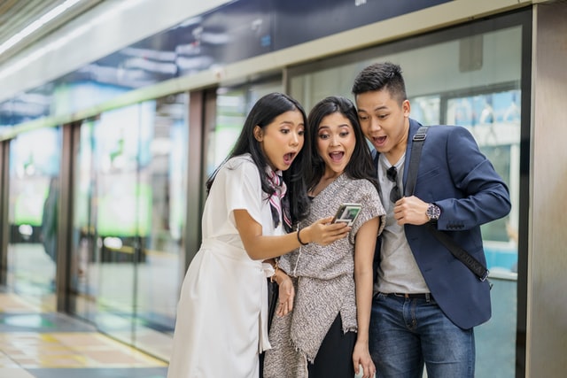 Three people act surprised as they look at a smartphone.