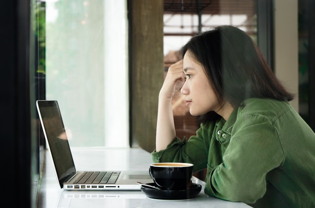 A woman wearing a green jacket looks at a laptop in a cafe.