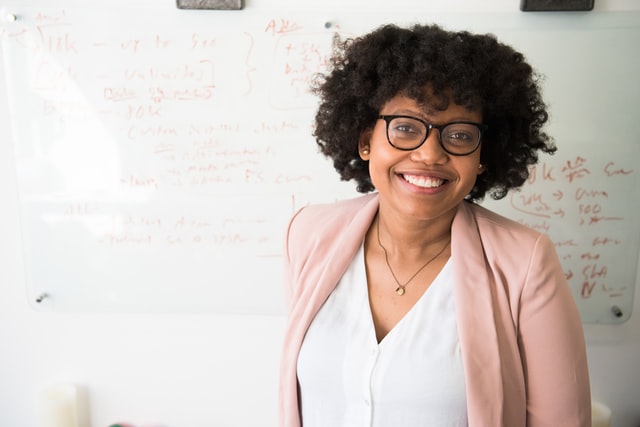 A woman in a peach sports jacket and glasses smiles at the camera.