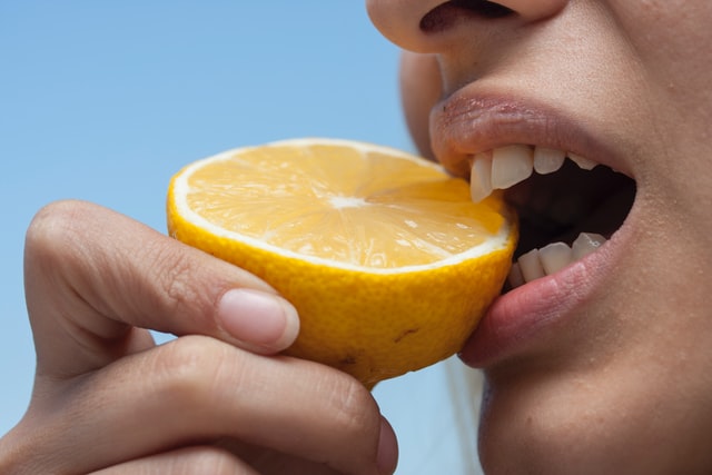 A person holding and biting into a lemon wedge.