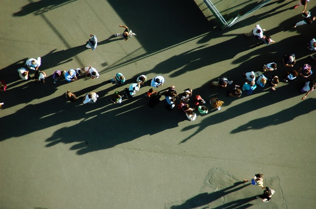 A large group of people stands in line outside.