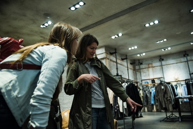 A woman points out clothing on a rack to another woman.