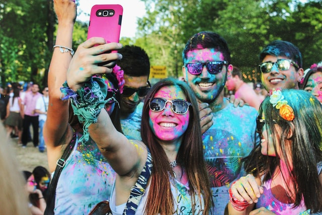 A group of people covered in colorful powder takes a selfie.