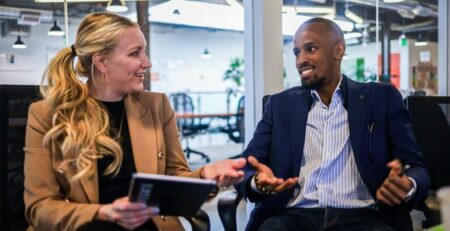 A man and a woman sit in a meeting room talking.