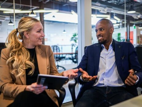 A man and a woman sit in a meeting room talking.