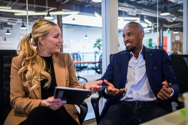 A man and a woman sit in a meeting room talking.