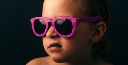 A kid in pink sunglasses grimaces away from the camera.