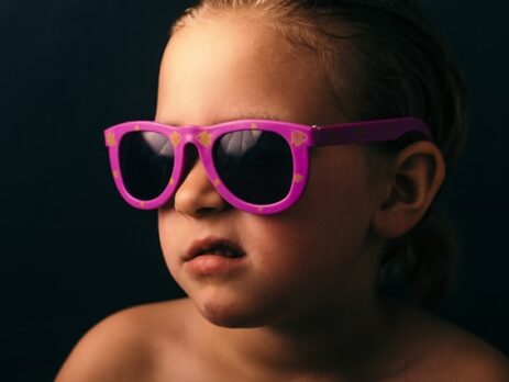 A kid in pink sunglasses grimaces away from the camera.