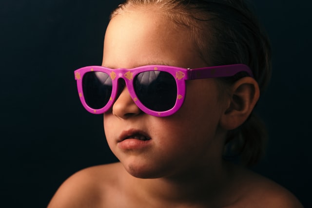 A kid in pink sunglasses grimaces away from the camera.