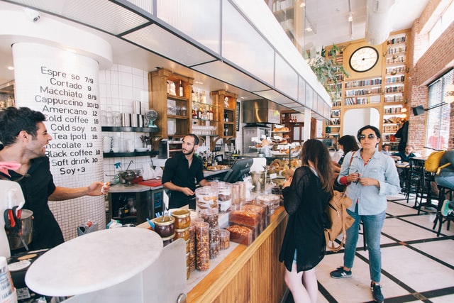 Customers stand in front of the cash register at a coffee shop.