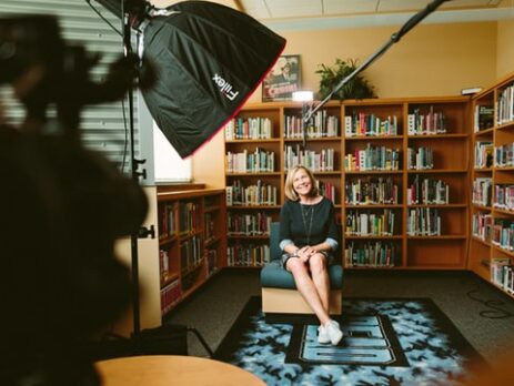 A crew filming an interview with a woman in a library.