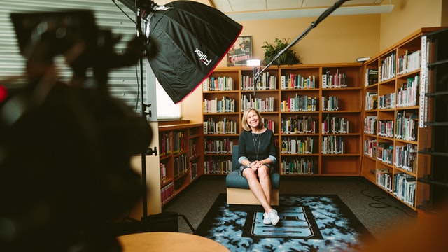 A crew filming an interview with a woman in a library.