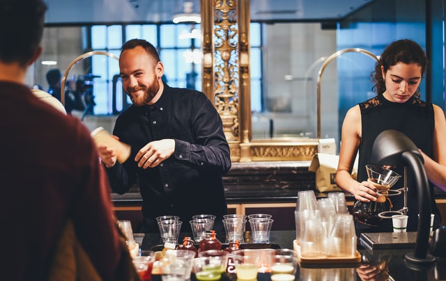 A bartender smiles at a customer as he shakes a mixer.