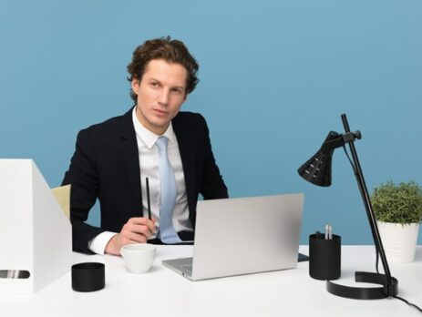 A man sits behind a desk thinking.