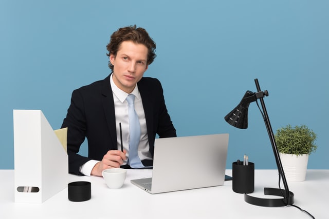 A man sits behind a desk thinking.