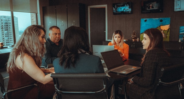 Five people talk around a table filled with laptop computers.