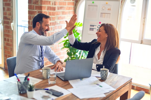 A man and a woman in business attire having a high five.