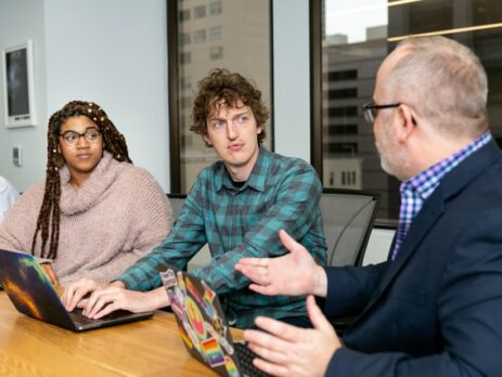 Three people have a discussion around a conference table.