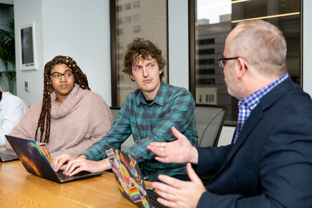 Three people have a discussion around a conference table.