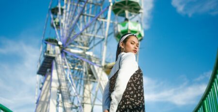 A woman looks over her shoulder at the camera in front of a ferris wheel.