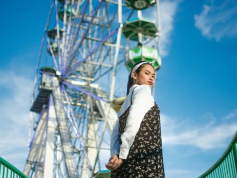 A woman looks over her shoulder at the camera in front of a ferris wheel.