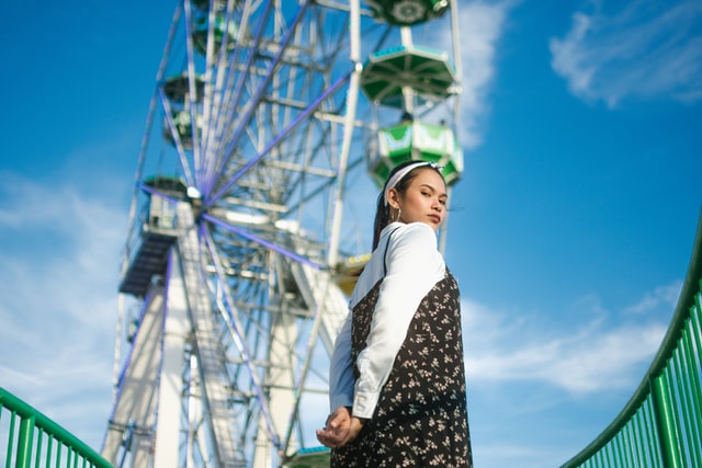 A woman looks over her shoulder at the camera in front of a ferris wheel.