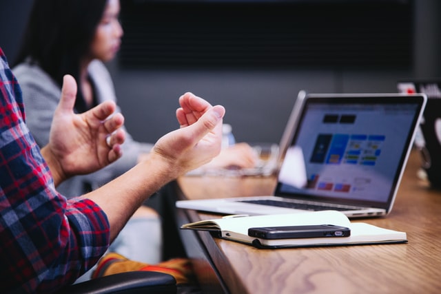A man talks with his hands while a laptop is open on the desk.