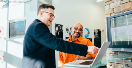 A man points at something on a computer while another man looks.