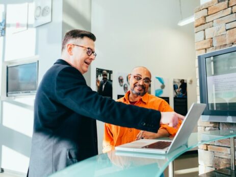 A man points at something on a computer while another man looks.