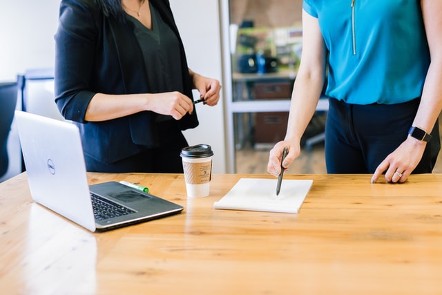 Two women use a computer and make notes prior to a negotiation.