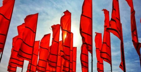 Several red flags flying against a blue sky.