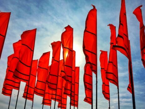 Several red flags flying against a blue sky.